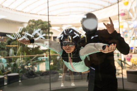 Aufgeregtes Teenager-Mädchen mit Helm fliegt im aerodynamischen Röhren-Windkanal. Fallschirmsprungtraining. Hochwertiges Foto