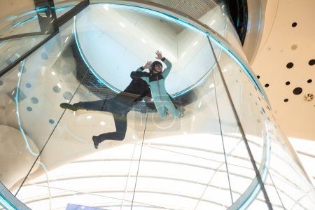 Excited teenage girl in helmet flying in aerodynamic tube wind tunnel. Skydiving training. High quality photo