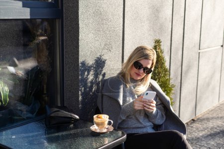 Middle aged woman entrepreneur with smartphone sitting in a street cafe. . High quality photo