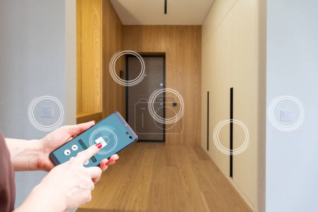 Smart home automation app on smartphone hold by female hand with home interior in background.