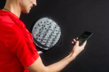 man holding paddel racket and smartphone with bet black background. High quality man holding padel racket and smartphone with bet black background