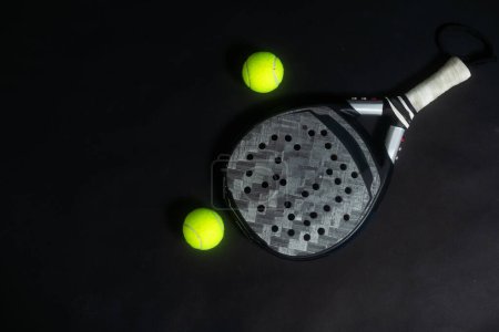 Detailed background of black and white padel racket and ball on black background. Top view. High quality photo