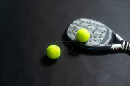 Detailed background of black and white padel racket and ball on black background. Top view. High quality photo