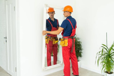 Téléchargez les photos : Man installing a mirror on wall. - en image libre de droit