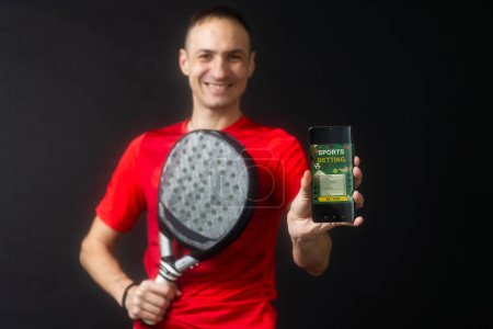 man holding paddel racket and smartphone with bet black background. High quality man holding padel racket and smartphone with bet black background