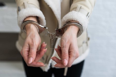 A woman who has been arrested and has her hands handcuffed behind her back to the rear. The prisoner is awaiting transport to the jail. High quality photo