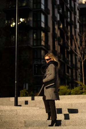 Téléchargez les photos : La fille en manteau se promène dans la ville par une journée ensoleillée. Photo de haute qualité - en image libre de droit