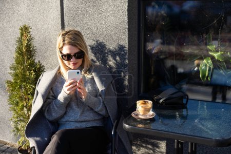 Femme d'âge moyen entrepreneur avec smartphone assis dans un café de rue. . Photo de haute qualité