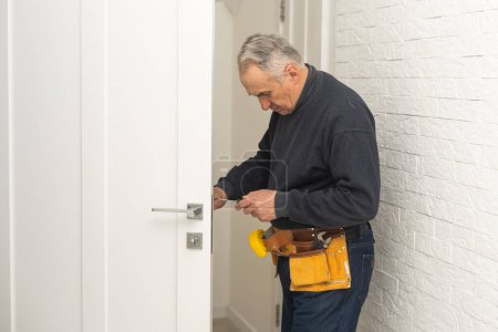 Foto de Ordinary elderly man independently repairs a door. - Imagen libre de derechos