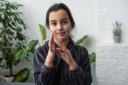 Cute deaf mute girl using sign language on light background.