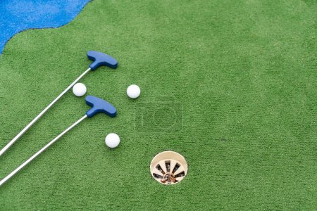 Mini-golf clubs y pelotas de diferentes colores colocados sobre césped artificial. Foto de alta calidad