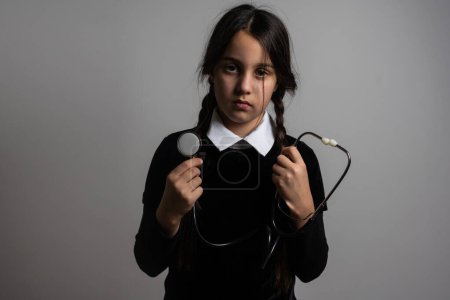 A girl with braids in a gothic style on a dark background with stethoscope
