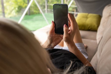 Happy young caucasian woman relax on comfortable couch at home texting messaging on smartphone, use cellphone, browse wireless internet on gadget, shopping online from home.