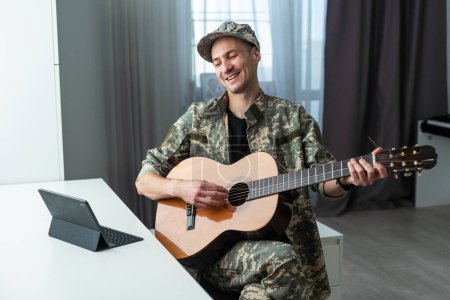 Cheerful smiling young military man wearing khaki uniform holding guitar. High quality photo