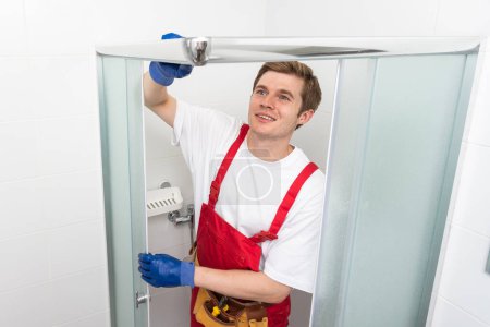 Jeune homme réparant porte de cabine de douche dans la salle de bain
