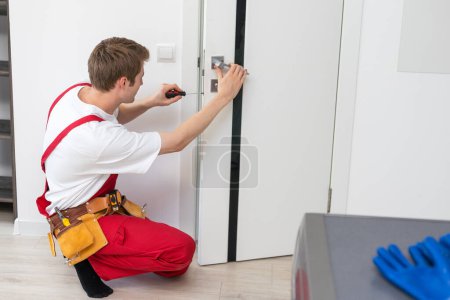 Téléchargez les photos : Jeune homme fixer la porte dans la maison. - en image libre de droit