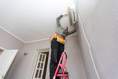 Técnico masculino limpiando aire acondicionado en interiores. Foto de alta calidad
