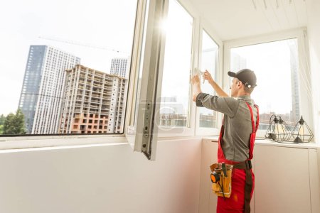 Photo for Maintenance man is fixing windows in a living room using a skrewdriver. He is wearing glasses, yellow gloves and a black apron. High quality photo - Royalty Free Image