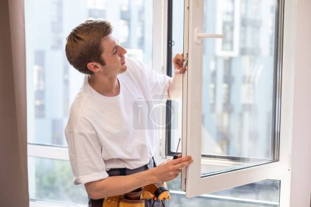 Photo for A repairman repairs, adjusts or installs metal-plastic windows in the apartment. glazing of balconies, loggias, verandas in house. production of double-glazed windows to individual sizes. - Royalty Free Image