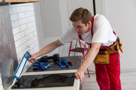 Téléchargez les photos : Craftsman installs hob in kitchen. Household Appliance Installation Services Concept - en image libre de droit