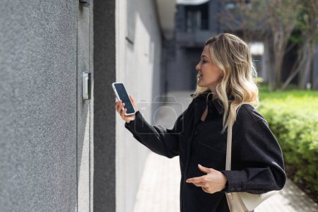 Lächelnde Frau, die mit Hilfe einer mobilen Anwendung ein Sicherheitssystem für ihr Haus einrichtet. Hochwertiges Foto