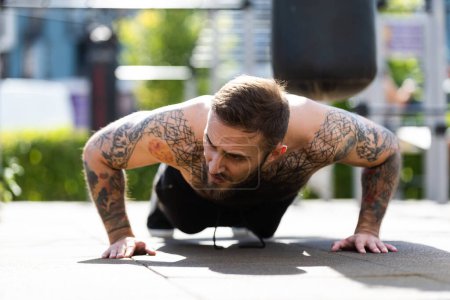 Muskulöser Bodybuilder schöner Mann mit nacktem Oberkörper trainiert Trizeps in einem Crossover-Kabeltrainingsgerät auf der Straße.