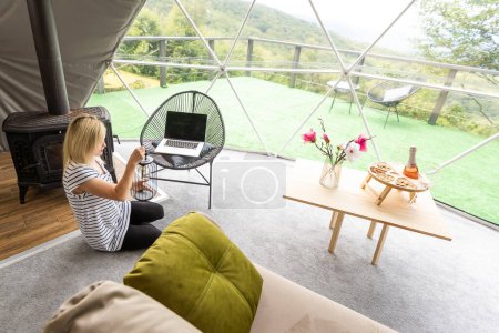 Glückliche junge Frau chattet online mit dem Laptop im Kuppelzelt. Glamping-Urlaubskonzept.