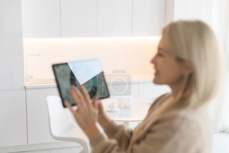Mujer controlando dispositivos domésticos inteligentes utilizando una tableta digital con aplicación lanzada en la sala de estar blanca. Concepto de hogar inteligente
.
