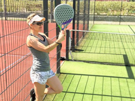 Foto de Retrato de mujer emocional activa jugando padel tenis en pista abierta en verano, balanceo raqueta para devolver la pelota sobre la red.. Foto de alta calidad - Imagen libre de derechos