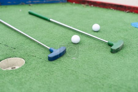  Mini-golf clubs and balls of different colors laid on artificial grass. High quality photo