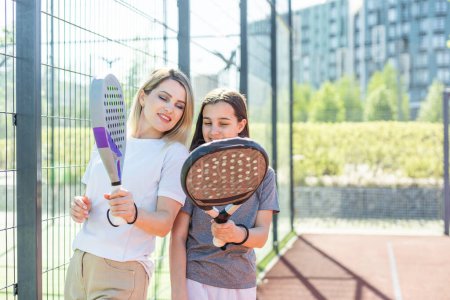 Fröhlicher Trainer, der dem Kind Padel-Tennis beibringt, während beide auf dem Tennisplatz stehen. Hochwertiges Foto