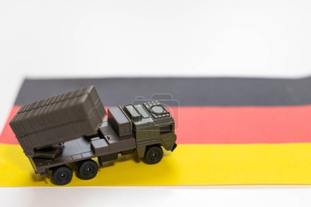 Krieg, militärische Bedrohung, militärisches Machtkonzept. Deutschland. Panzerspielzeug in der Nähe der deutschen Flagge auf schwarzem Hintergrund von oben. Hochwertiges Foto
