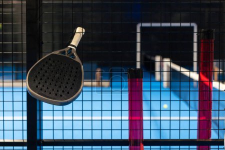 Black professional paddle tennis racket and ball with natural lighting on blue background. Horizontal sport theme poster, greeting cards, headers, website and app. High quality photo
