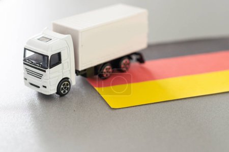 Mini-Spielzeug am Tisch mit verschwommenem Hintergrund. Industrieschifffahrtskonzept. Spielzeugwagen, Deutschland-Fahne. Hochwertiges Foto