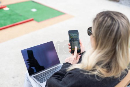 Frau auf Golfplatz mit Smartphone mit Sportwetten-App Hochwertiges Foto