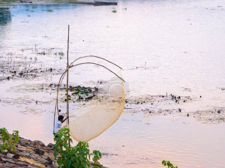 Téléchargez les photos : Balasore, Odisha, Inde, 26 octobre 2023. Un jeune garçon rural non identifié attrapant du poisson avec résille sur un lac. - en image libre de droit