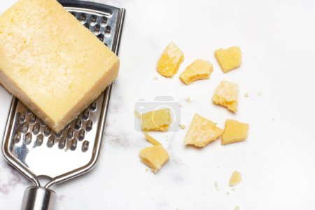 Foto de Un trozo de queso parmesano en un rallador de queso en un mostrador de mármol blanco y gris - Imagen libre de derechos