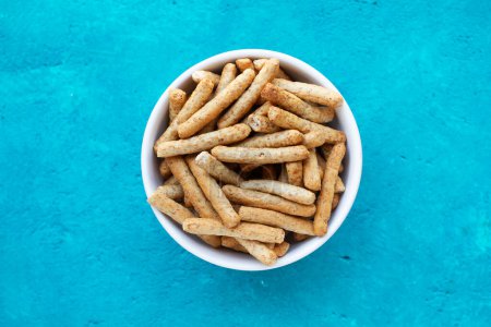 Small breadsticks in a white bowl on a blue background in a top view