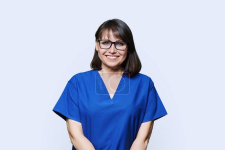 Lächelnde Frau in blauer Peeling-Uniform blickt in die Kamera auf weißem Studiohintergrund. Ärztin Krankenschwester Laborantin Apothekerin Tierärztin medizinische Fachangestellte