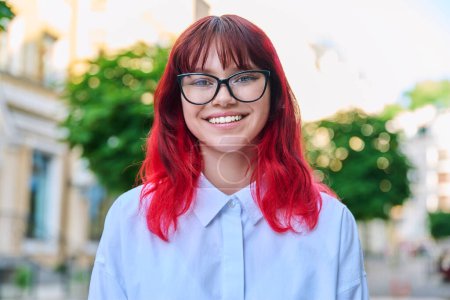 Photo for Headshot portrait of positive teenage young female in glasses looking at camera. Beautiful fashionable teenager girl with red dyed hair in city. Beauty, hair, youth, fashion, young people concept - Royalty Free Image
