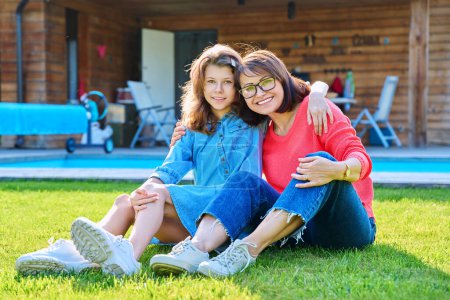 Photo for Portrait of happy mom and teenage daughter looking at camera. Smiling hugging mother and girl together in backyard near outdoor pool. Family, parent and child teenager, mothers day, lifestyle concept - Royalty Free Image