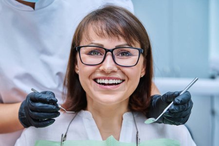 Photo for Close-up face of smiling mature woman with teeth in dentistry with hands with dentist examination tools. Treatment, prosthetics, implantation, whitening, hygiene, dental health care concept - Royalty Free Image