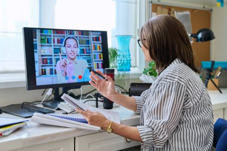 Mature woman talking online with teenage girl using video call on computer, home interior. Virtual meeting, therapy session with psychologist. Chat conference technology psychology education learning