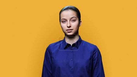 Photo for Portrait of serious teenage girl 15, 16 years old, calm young female looking at camera on yellow color studio background. Adolescence, high school education, lifestyle, beauty health concept - Royalty Free Image