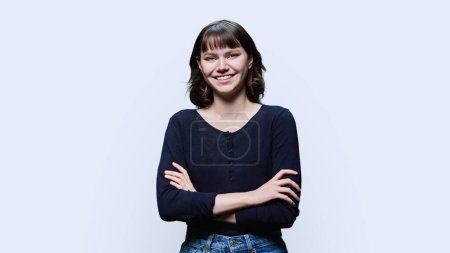 Portrait of young smiling female looking at camera, with crossed arms on white studio background. Happy cheerful positive female 18, 19 years old. Lifestyle, youth concept