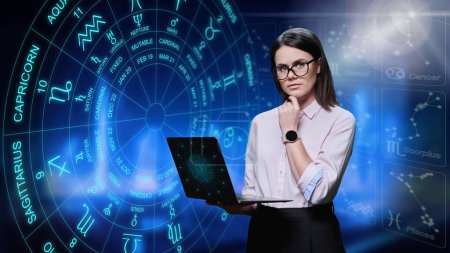 Young woman with laptop looking at camera, astrological symbols and signs background. Horoscope, zodiac signs, astrology, numerology, forecast service concept