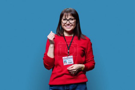 Middle-aged woman mentor teacher with id card badge of employee of educational center, on blue background. Administrative organizational work, education, training, teaching concept