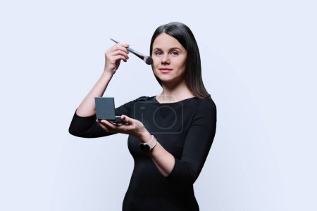 Photo for Young woman holding compact powder and using makeup brush, on white studio background. Attractive female posing with brush in hands, beauty cosmetics advertising, decorative cosmetics, fashion concept - Royalty Free Image