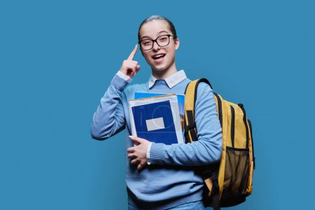 Téléchargez les photos : Portrait d'une adolescente lycéenne sur fond de studio bleu. Femme souriante en chandail avec sac à dos regardant la caméra. Éducation, adolescence, biens et services pour adolescents - en image libre de droit