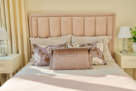 Photo for Classic trendy bedroom interior in light ivory colors, in warm sunlight, pink double bed with sofa cushions, bedside tables with lamps. Comfort, home, style, decor, design concept - Royalty Free Image